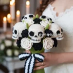 A woman in a wedding dress holds a crocheted bouquet featuring skulls and black and white roses, with a black and white ribbon tied around the stem, set against a softly lit background with candles.