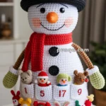 A crocheted snowman with a black hat, red scarf, and colorful mini plush toys in numbered pockets on its body, functioning like an advent calendar.