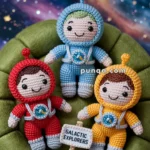Three crocheted astronaut dolls wearing blue, red, and yellow spacesuits sit on a green cushion against a starry galaxy background, with a small sign reading "Galactic Explorers."