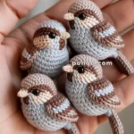 A human hand holding four intricately crocheted miniature birds in shades of brown and grey.