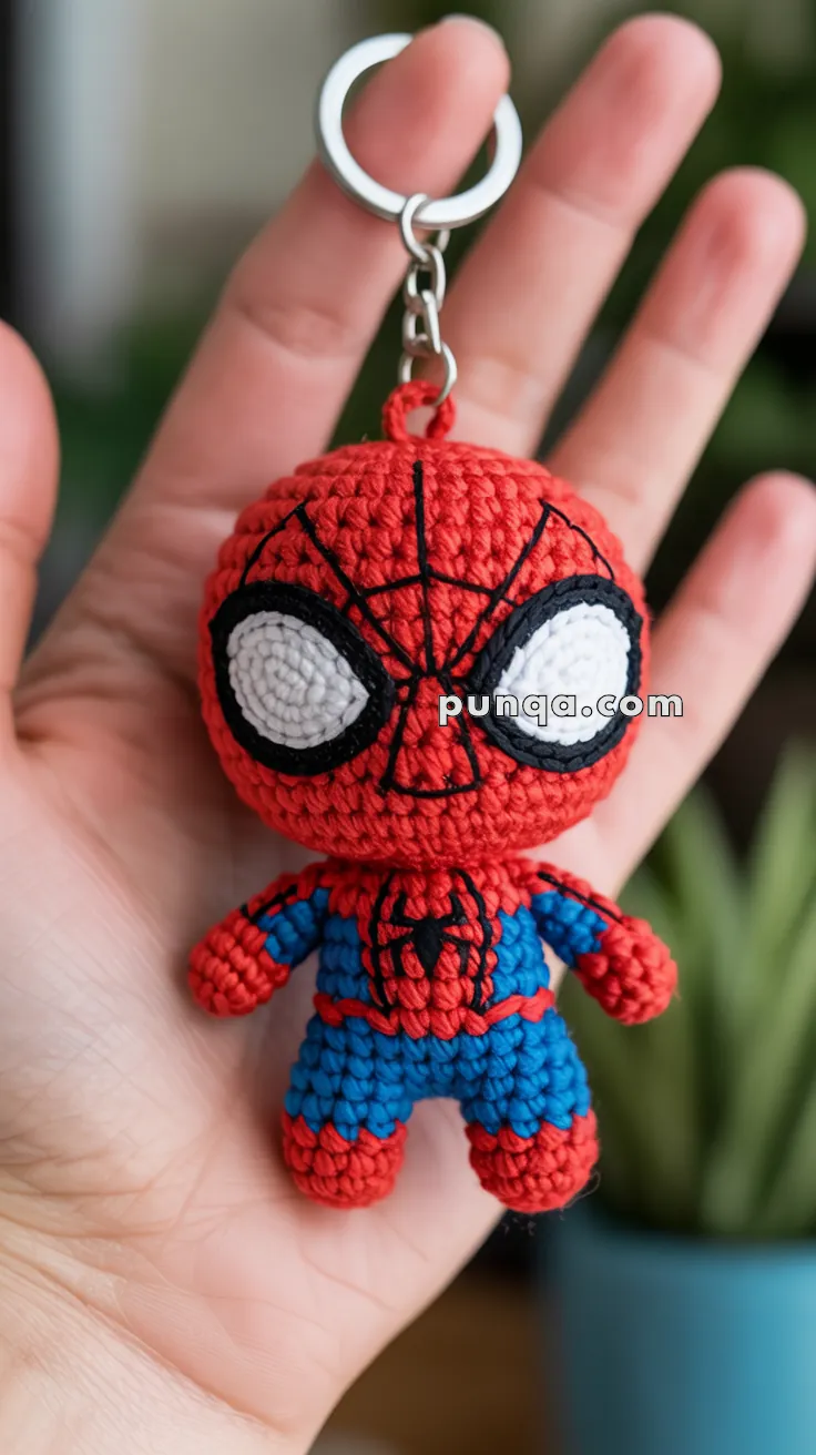 A handmade crochet keychain featuring a small figure in red and blue resembling a well-known superhero, held in the palm of a hand.