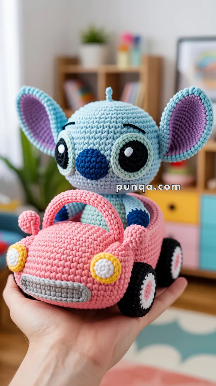 A crocheted toy featuring a light blue character with large ears and a pink nose, sitting inside a pink crocheted car held by a person's hand. The setting is indoors with a blurred background of shelves and a plant.