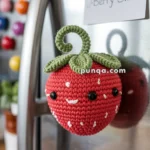 Crocheted strawberry magnet with cute face and green leaves attached to a refrigerator door, next to a note card reading 'Berry Sweet.'