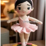 A crocheted doll in a ballet pose, wearing a pink tutu and matching ballet shoes, is displayed on a round crocheted base adorned with pink and yellow flowers.
