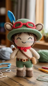 Crocheted doll with a green hat, red glasses, blue feather, and brown bag, smiling with closed eyes on a wooden table.