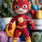A knitted doll resembling a superhero, featuring a red and yellow outfit with a lightning bolt emblem, standing on a wooden surface with colorful yarn balls and knitting tools in the background.