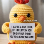 A crocheted yellow chick holding a sign that says, "I may be a tiny chick, but I believe in you. Go do your thing! You're cluckin' awesome!" The chick has orange feet and a small orange beak.