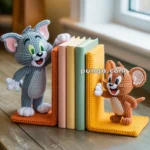 Crocheted bookends featuring a gray cat and a brown mouse with three books between them on a wooden table by a window.