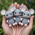 Three crocheted gray mice with pink ears and noses held in hands, with a green foliage background.