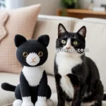 A black and white cat sits on a couch next to a matching crocheted toy cat with similar colors and facial features.