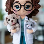 A crocheted doll dressed as a veterinarian with curly brown hair and large glasses, holding a small crocheted dog and cat, wearing a white lab coat over teal scrubs.