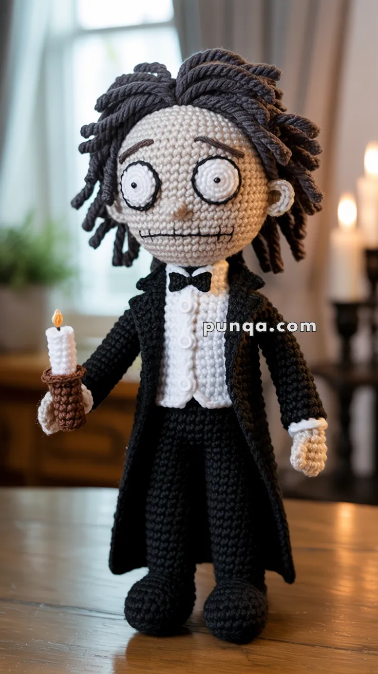 Crochet doll with black hair and wide eyes, dressed in a black tuxedo with a white shirt and bow tie, holding a crocheted candle.