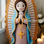 Crocheted figure of a woman with folded hands, wearing a blue cloak, surrounded by a golden halo and white crochet beads.