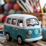 A crocheted model of a classic Volkswagen van, featuring a blue and white color scheme and intricate detailing, placed on a wooden surface with colorful yarn and crochet hooks in the background.