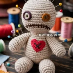 A handmade crochet voodoo doll with mismatched button eyes and a stitched mouth, used as a pincushion with colorful pins in its head and body. It features a red heart decoration on its chest and is surrounded by sewing materials like threads and scissors on a wooden table.
