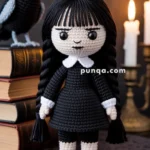 A crocheted doll with braided black hair and a black dress with a white collar, standing on a table beside a stack of books and a crocheted raven, with lit candles in the background.
