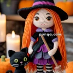 Crocheted doll dressed as a witch with orange hair and a black hat, standing next to a black crocheted cat, surrounded by pumpkins and candles.