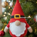 A crocheted gnome ornament with a red hat, white beard, and black boots, hanging on a decorated Christmas tree.