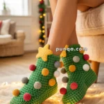 A person wearing green, knitted slipper socks designed to resemble Christmas trees, complete with colorful pom-pom 'ornaments' and a yellow star on top. The setting is a cozy room with festive holiday decorations.