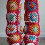 A pair of legs wearing colorful crocheted leg warmers featuring square patterns in blue, pink, green, and orange over white platform shoes.