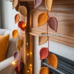 Crocheted leaf garland in autumn colors draped over a fireplace mantel with glowing string lights.