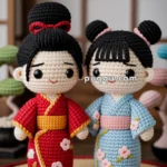 Two amigurumi dolls wearing traditional Japanese kimonos stand on a woven mat. The doll on the left wears a red kimono with a yellow trim and floral patterns, with a red hair bow. The doll on the right wears a blue kimono with a pink obi and matching floral patterns. Both dolls have black hair styled in buns.