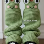 Green crochet leg warmers designed to resemble whimsical frogs with eyes and smiles, worn above black shoes adorned with white daisy embellishments.