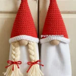 Two kitchen towels designed like gnome figures, with red crocheted hats and white fabric bodies; the left one features braided hair tied with red bows.