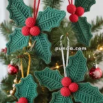 Crocheted green holly leaves with red berries hanging as ornaments on a Christmas tree.