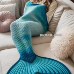 A woman sitting on a sofa, wrapped in a blue and teal mermaid tail blanket, with a cozy fireplace in the background.