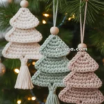 Three crochet Christmas tree ornaments in cream, green, and pink hanging on a pine tree with a beaded loop.