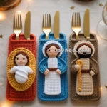 Three crocheted utensil holders resembling nativity figures containing gold knives and forks, placed on a decorated table with candles and pine branches.
