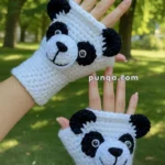 Two hands wearing crocheted white and black panda-themed fingerless gloves, with a forest background.
