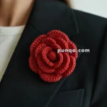 A person wearing a black blazer with a large red crocheted flower brooch pinned on the lapel.