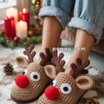 A pair of feet wearing crocheted reindeer slippers with bright red noses and antlers, surrounded by pinecones on a soft surface, with lit candles and festive decorations in the background.