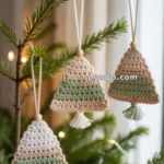Crochet Christmas tree ornaments in beige and green tones, hanging on a decorated branch with small lights.
