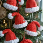 A Christmas tree adorned with crocheted Santa hat ornaments featuring red tops and white brims and pompoms, hanging from colorful strings.