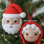 Crocheted Christmas ornaments depicting Santa Claus and Mrs. Claus hanging on a Christmas tree with pine branches and soft lights.