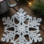 A wooden table decorated with a crocheted white snowflake, a mug of hot chocolate, and evergreen branches with string lights.