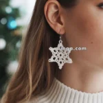 A close-up of a person wearing a white star-shaped crocheted earring, with a blurred background showing part of a green and blue decorated tree.