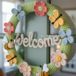 A handmade crochet wreath with colorful flowers and bees, featuring a "Welcome" sign, hanging on a door.